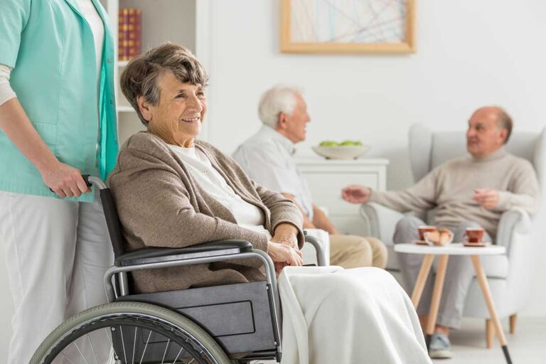 Four older adults participating in a group stretching exercise with a fitness instructor in a bright room.